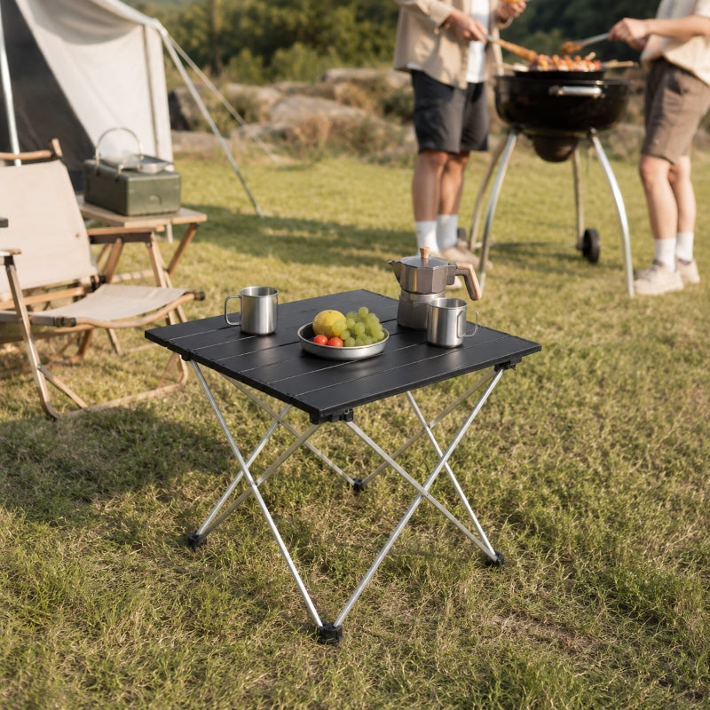Folding camping table with aluminium top holding food and drinks at outdoor barbecue