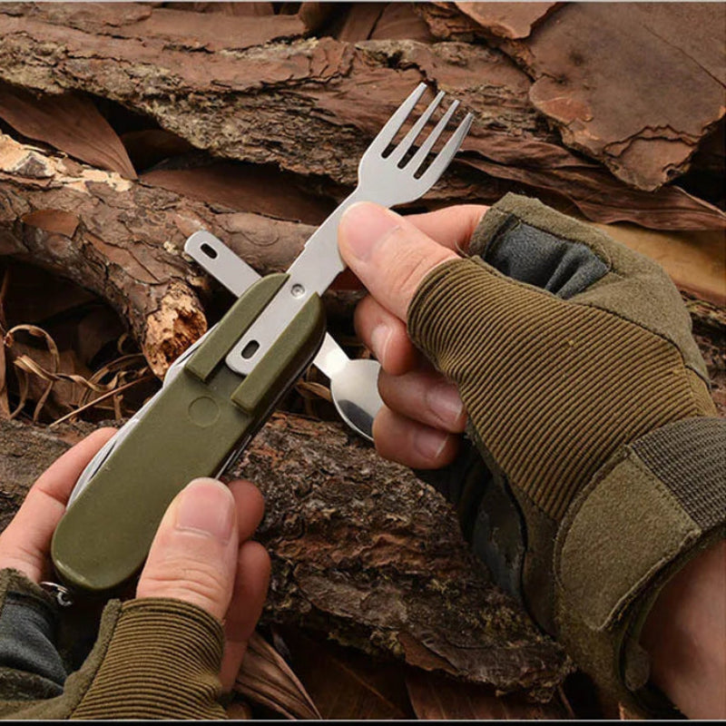 Hands wearing fingerless gloves using a green camping cutlery multitool with detachable stainless steel fork and spoon against a tree bark background, demonstrating outdoor meal use