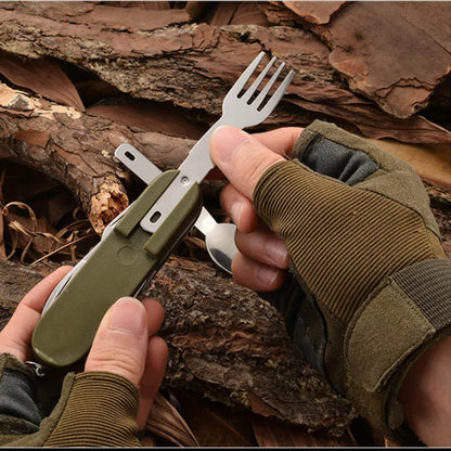 Hands wearing fingerless gloves using a green camping cutlery multitool with detachable stainless steel fork and spoon against a tree bark background, demonstrating outdoor meal use
