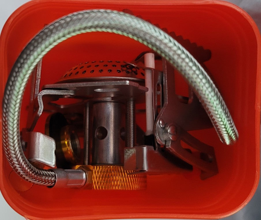 Close-up of a camping stove with a hose inside an orange container