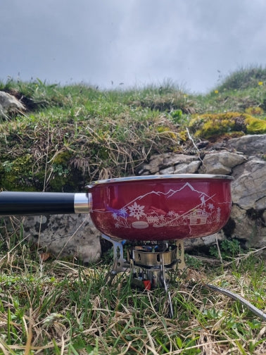 Red camping stove with mountain design on a grassy hillside