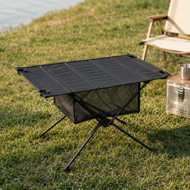 Person using folding camping table outdoors with mug and gear on top
