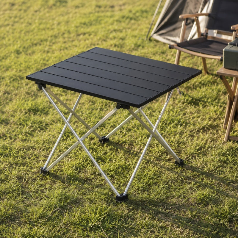 Folding camping table with aluminium top set up on grass next to tent and camping chair