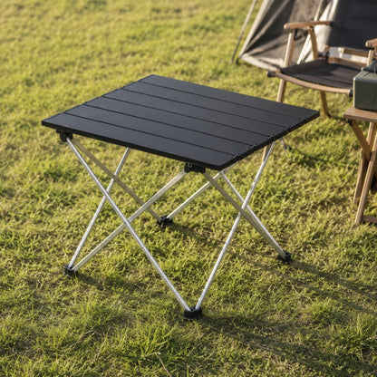 Folding camping table with aluminium top set up on grass next to tent and camping chair