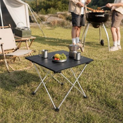 Folding camping table with aluminium top holding food and drinks at outdoor barbecue