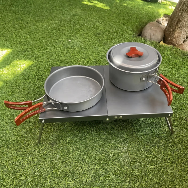 Ultralight folding camping table in black on grass with cookset, close-up angle