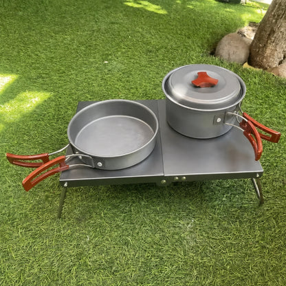 Ultralight folding camping table in black on grass with cookset, close-up angle