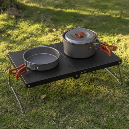 Ultralight folding camping table in black set up on grass with camp cookset